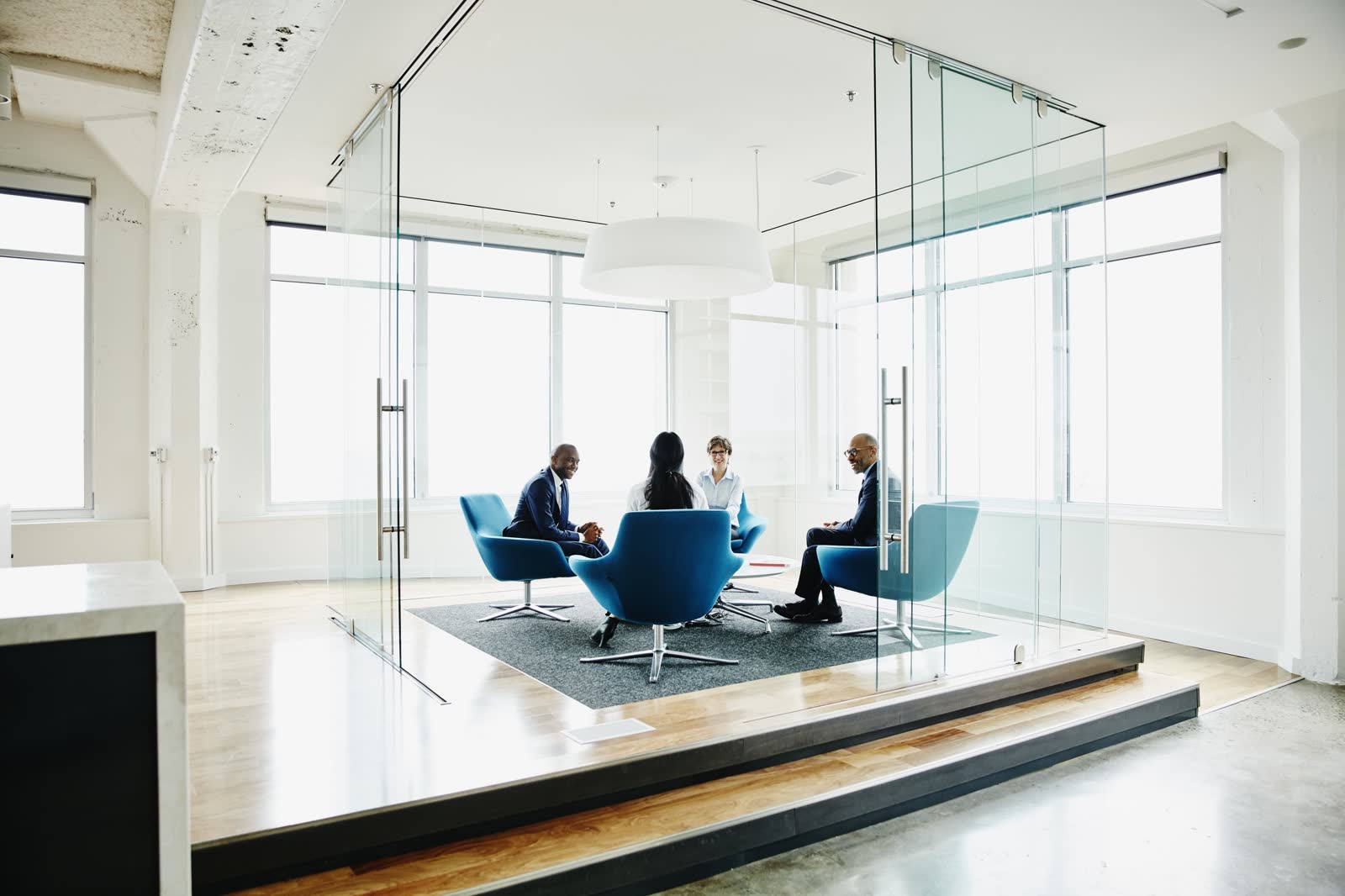 Four business professionals meeting in a glass conference room